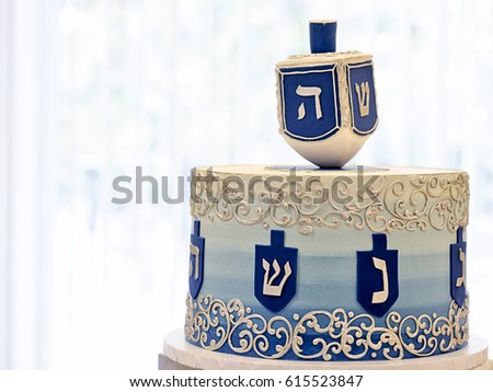 Close up of  Chanukah dreidel cake in blue silver and white buttercream and fondant icing for  Jewish holiday Chanukah or Hanukkah with a subtle blue and white cool winter  background and copy space