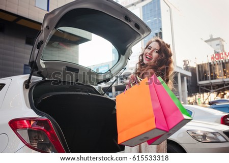 Beautiful young girl stands near a car with bags, makes a shopping