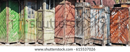 It is the line of aged vintage cracked wooden old doors of rural sheds. Spring sunny day. Panoramic image from several photos. 