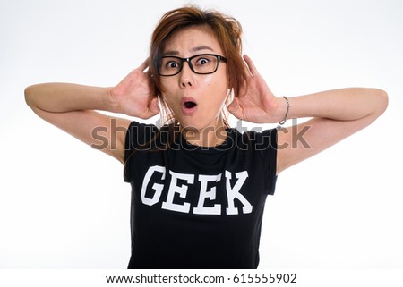 Studio shot of young Asian geek girl looking shocked and listening on both sides while wearing eyeglasses against white background