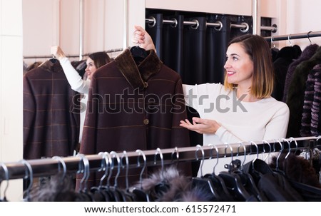 Pretty woman customer chooses a warm sheepskin coat in a cloths store