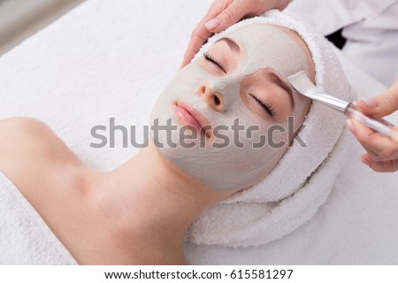 Face peeling mask, spa beauty treatment, skincare. Woman getting facial care by beautician at spa salon, side view, close-up Royalty-Free Stock Photo #615581297