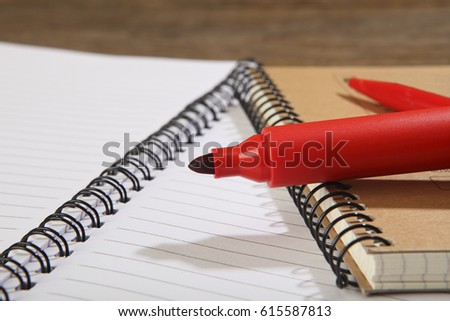 A red marker and a ballpoint pen lie on school notebooks. Close-up