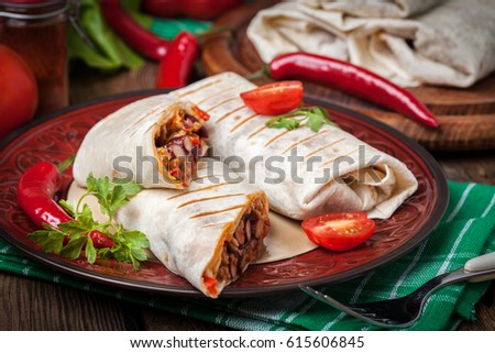 Burritos wraps with meat, beans and vegetables on wood board. Shallow depth of field.