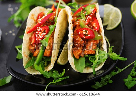 Mexican tacos with chicken fillet in tomato sauce and salsa of paprika and arugula.