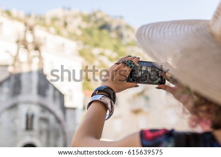 Attractive woman in colorful dress wearing sunhat taking a photo using smart phone in a small coastal old town on a sunny summer day