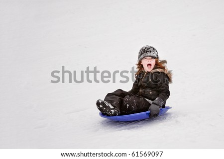 A girl sledding down a hill, very excited.