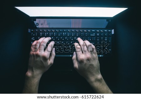 The hacker hacks the server with bank accounts in a dark room on a black background in the dark.  Royalty-Free Stock Photo #615722624