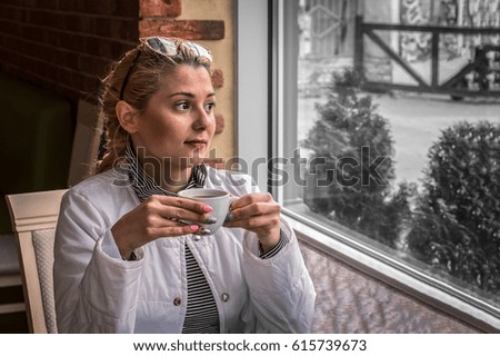 girl drinks coffee in a restaurant and looks out the window