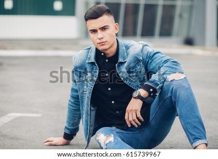 Stylish guy, sitting on the pavement in the denim jacket, men's looks