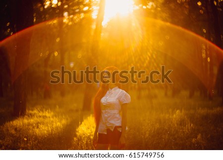 Beautiful young woman with red hair in the park. Sunlight. Portrait of a smiling red-haired girl in a park in the last rays. Very beautiful portrait of a redheaded girl in a park at sunset