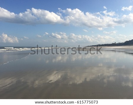 Reflections of puffy white clouds on the beach on a beautiful blue day. 