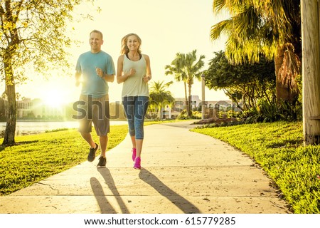 Man and woman exercising and jogging together at the park. Happy and smiling as they run along the path during sunset on a warm summer day Royalty-Free Stock Photo #615779285