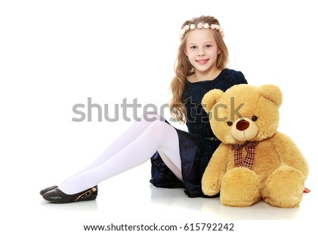 Beautiful little girl in a blue dress is hugging a large Teddy bear . Girl sitting on the floor.Isolated on white background.
