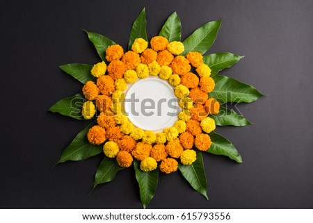 flower rangoli made using marigold or zendu flowers and mango leaves over black background with copy space in the middle, selective focus