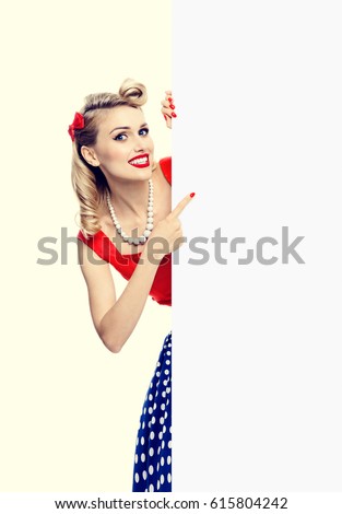 Happy smiling woman in pin-up style dress, showing blank signboard with copyspace. Caucasian blond model posing in retro fashion and vintage concept studio shoot.