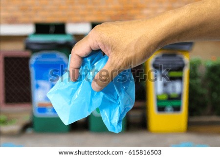 hand holding a blue plastic garbage against three garbage bins