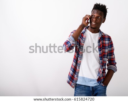 Studio shot of thoughtful young happy black African man smiling and talking on mobile phone while looking up against white background
