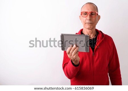 Studio shot of bald senior man using digital tablet while wearing eyeglasses against white background