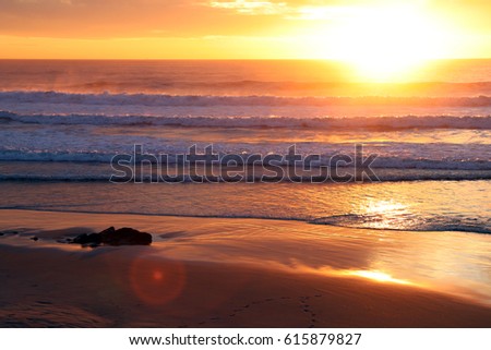 Beautiful blazing sunset landscape at Atlantic Ocean and orange sky above it with awesome sun golden reflection on waves as a background. Amazing summer sunset view on the beach