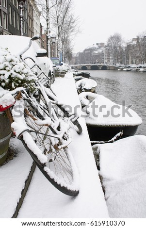 Usual bike in snow near the canal with boats in winter in Amsterdam