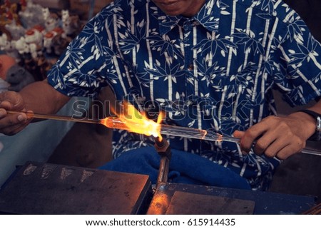 Workers are using the heat of gas blowing glass to look as art, shape, light, flame beautiful.