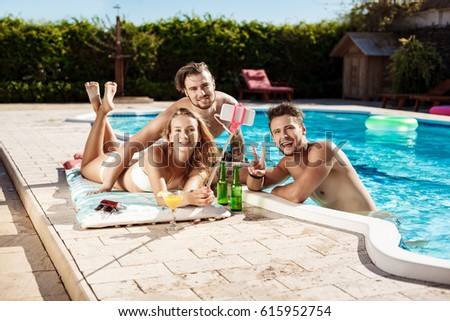 Friends smiling, making selfie, drinking cocktails, relaxing near swimming pool.