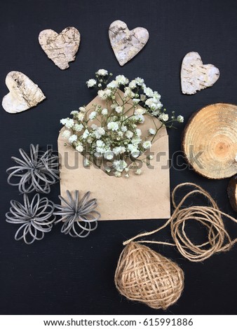gypsophila in craft envelope with bark hearts. rustic tiny white flowers in an envelope on black background.  
