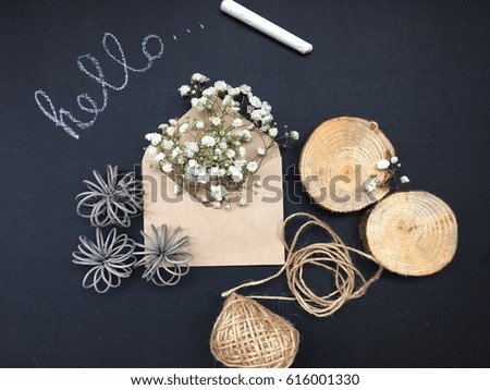 Small white flower in craft envelope. Craft gypsophila on black chalkboard. 