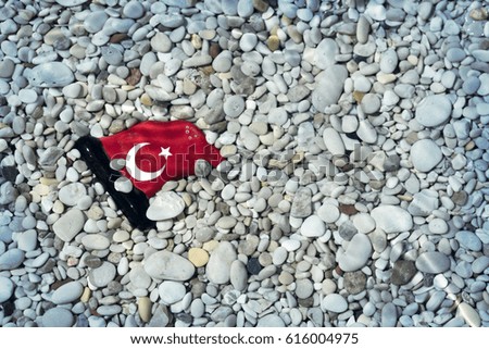 Small glossy ceramic Turkish flag lying in the gravel under water. Toned