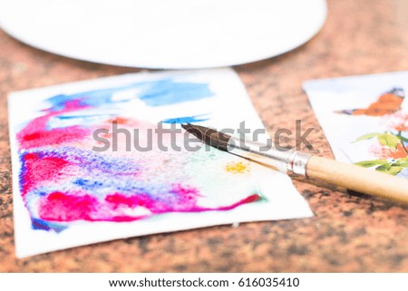 A set of watercolors is on the table. Next to it is a brush. A white sheet of paper.  Prepare and hold a master drawing class.Watercolor drawing. Real drawing. An example of drawing with watercolor.