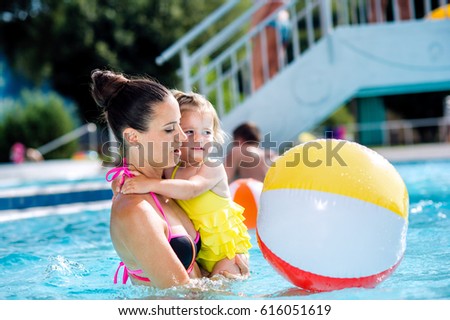 Mother with her daughter in swimming pool. Sunny summer.