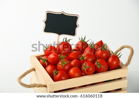 Fresh red ripe cherry tomatoes in small wooden box with black chalkboard price sign tag over white background