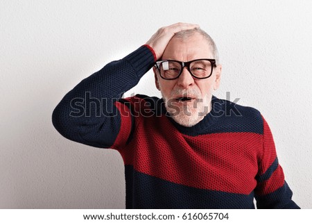 Upset senior man with headache, holding head, studio shot.