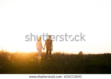 A loving couple walking in the field at sunset, holding each other's hands. The bright sunlight shines. Around the greens. Walk on the nature. Country style.
