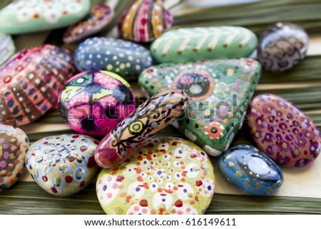Bright stones sea pebbles with a picture in ethnic, with a palm leaf, fashionable in a modern style, creative images, on a marble surface. Close-up