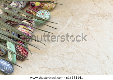 Bright stones sea pebbles with a picture in ethnic, with a palm leaf, fashionable in a modern style, creative images, on a marble surface