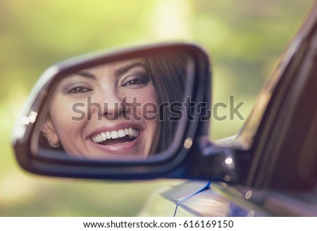 Happy young woman driver looking in car side view mirror, making sure lane is free before making a turn. Positive human face expression emotions. Safe trip driving concept Royalty-Free Stock Photo #616169150