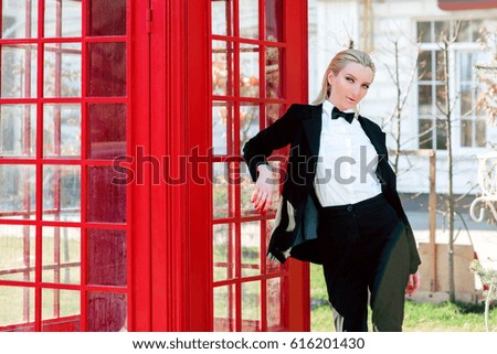 Portrait of stylish beautiful blonde woman in black suit near red telephone box