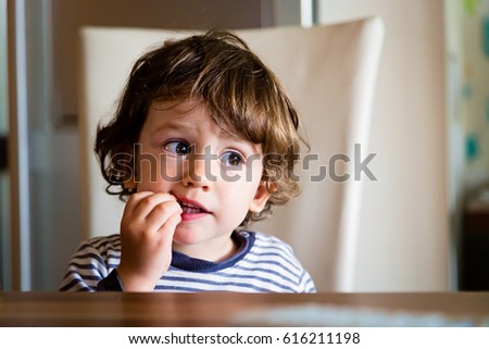 Little child toddler boy in the kitchen eating snack. Kid eats bread indoors. Royalty-Free Stock Photo #616211198