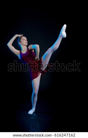 Young girl ballerina showing dance elements on a black background in blue scenic light