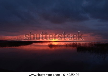 Gloomy sunset in the cloudy sky above the surface of the lake water
