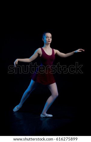 young ballerina girl dancer shows dance elements on a black background in a blue stage light