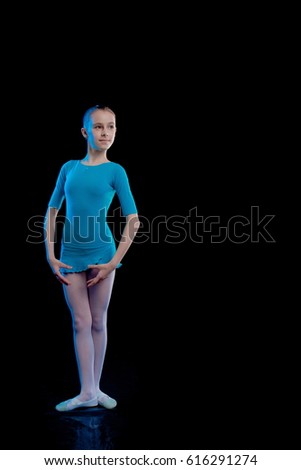Young girl ballerina showing dance elements on a black background in blue scenic light