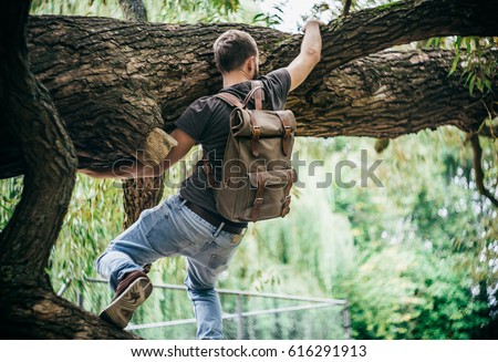 Young hipster man climbing on a tree in a park Royalty-Free Stock Photo #616291913