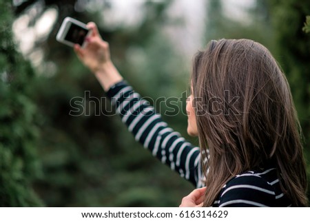 Young girl in striped sweater is taking picture of herself in the park. Shallow depth of field.