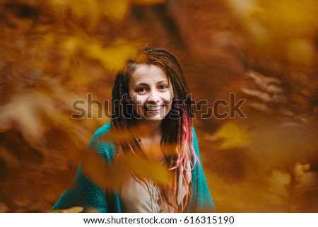 Young charming girl with dreads in a city Park on a bright day. Portrait of a girl with dreadlocks in the park. Looks at the camera and smiling in foliage