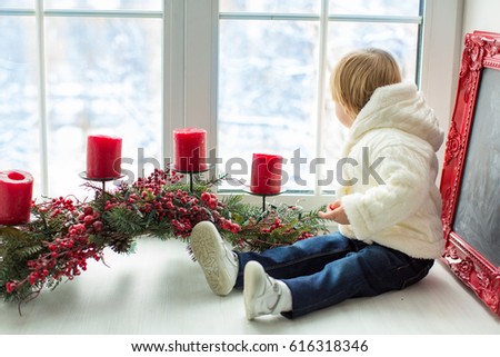 child sitting on the window sill looking into the window with Christmas decoration and candles