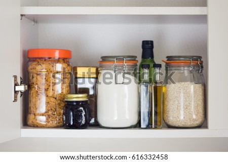 stocked kitchen pantry with food - jars and containers of cereals, jam, coffee, sugar, flour, oil, vinegar, rice Royalty-Free Stock Photo #616332458