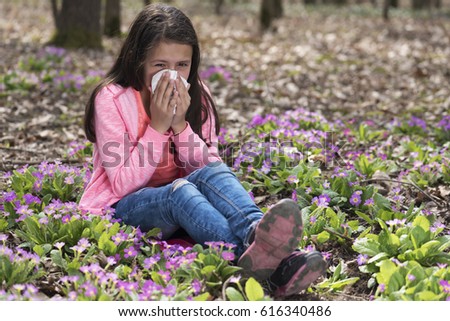 Cute girl blowing her nose among primroses. Selective focus  Royalty-Free Stock Photo #616340486